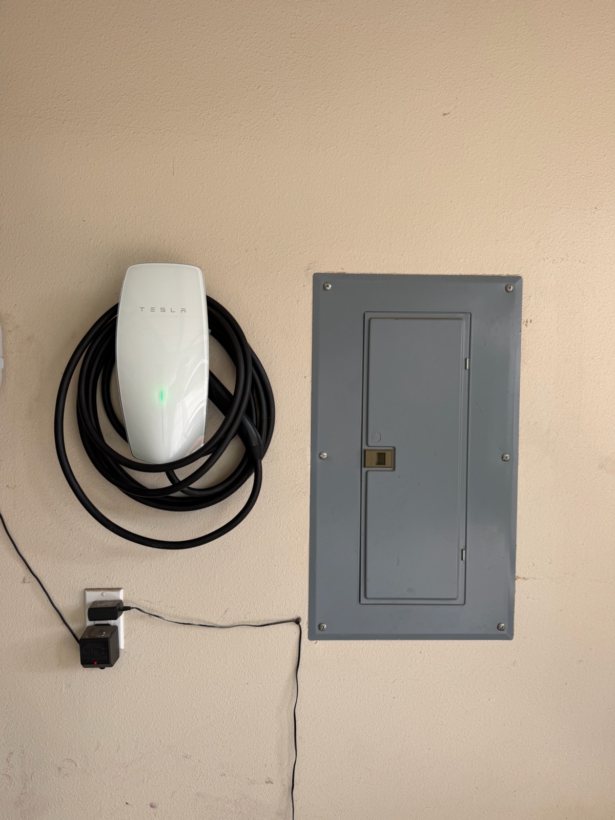 Tesla wall charger mounted beside a closed electrical panel.